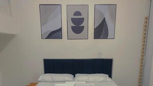 Una cama con una colcha blanca y roja, un cabecero oscuro y tres obras de arte abstracto en la pared superior.