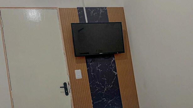 Habitación de hotel con cama, televisor de pantalla plana en la pared y aire acondicionado también fijado a la pared.