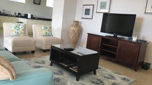 Ein Wohnzimmer mit einer Couch, Sesseln, einem Couchtisch, einem Fernseher und einem Schrank.