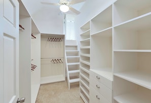 Ein begehbarer Kleiderschrank mit offenen Regalen, einer Leiter und einem Deckenventilator.