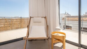 Un balcón con estructura de cama de madera, cortinas blancas y una pequeña mesa de madera con una lámpara.