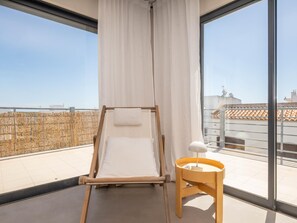 A balcony with a wooden bed frame, white curtains, and a small wooden table with a lamp. - Rivara Rooftop - Lux 3 Bedrooms (Cabanas de Tavira)