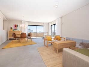 A modern living room with a dining area, large windows, and a view of the sea. - Rivara Rooftop - Lux 3 Bedrooms (Cabanas de Tavira)