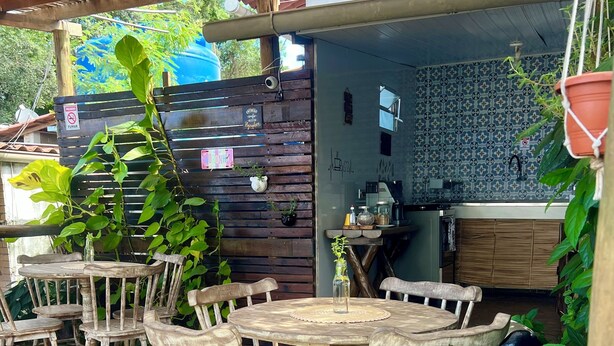 Una terraza de madera con una mesa redonda y sillas, un muro de ladrillo y una zona de cocina con salpicadero de azulejos.