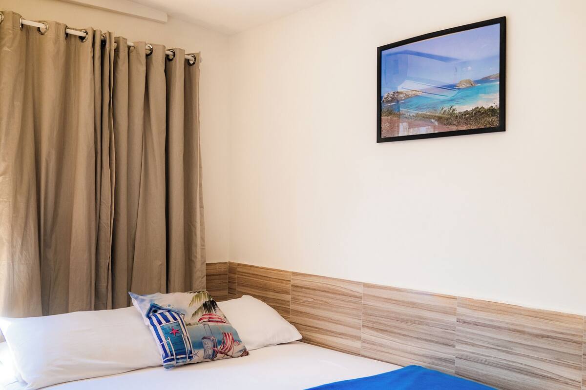 Una habitación de hotel con cama, cortinas, un cuadro y un cabecero de madera.