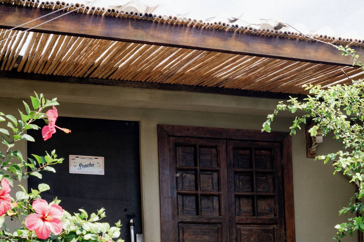 Un edificio rústico con puerta de madera, techo de bambú y un letrero que dice 'Pimcho'.