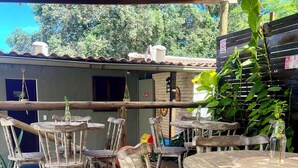 Un patio al aire libre con mesas y sillas de madera, un área cubierta y un edificio de ladrillo al fondo.