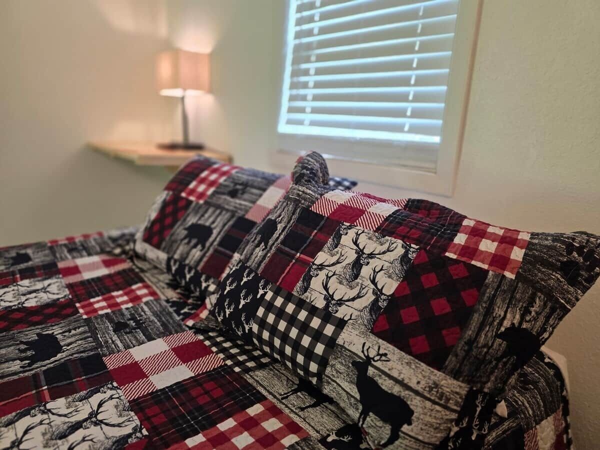 A bed with a checkered blanket and pillows with deer patterns.