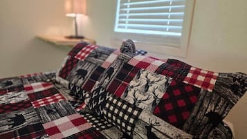 A bed with a checkered blanket and pillows with deer patterns.
