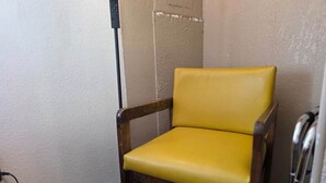 Una silla amarilla con apoyabrazos de madera en una habitación con pared texturizada y un enchufe a la vista.