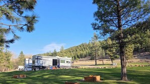 Una caravana de recreo en un área con césped, con árboles y una colina al fondo.