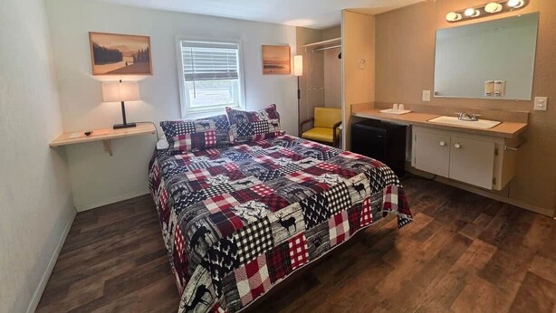 Un dormitorio con cama, mesitas de noche, una ventana, un espejo y un baño con lavabo y espejo.