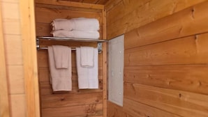 Ett badrum med träpanel på väggarna, en toalett, en hylla med hopvikta handdukar och en synlig toalettpappersrulle.