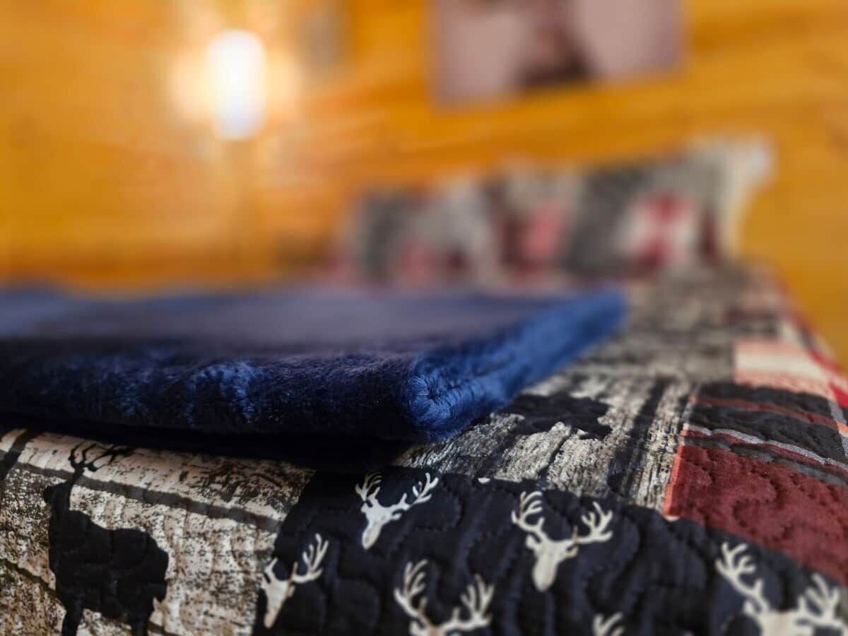 A bed with a patterned blanket and a blue pillow.
