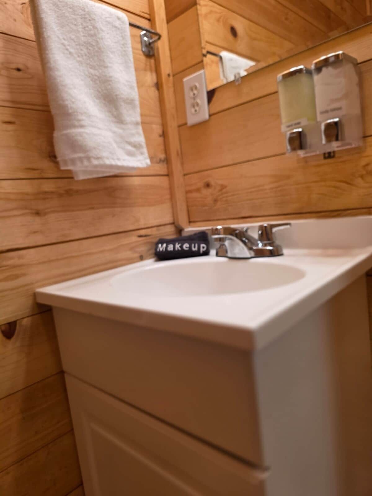 A wooden interior with a white sink, a towel hanging on a rack, and a mirror with soap dispensers.