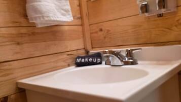 A wooden interior with a white sink, a towel hanging on a rack, and a mirror with soap dispensers.