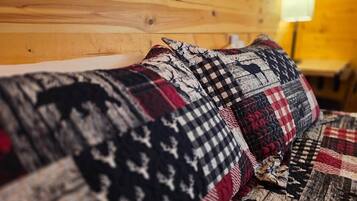 A bed with a patterned quilt and pillows, wooden headboard, and a lamp in the background.