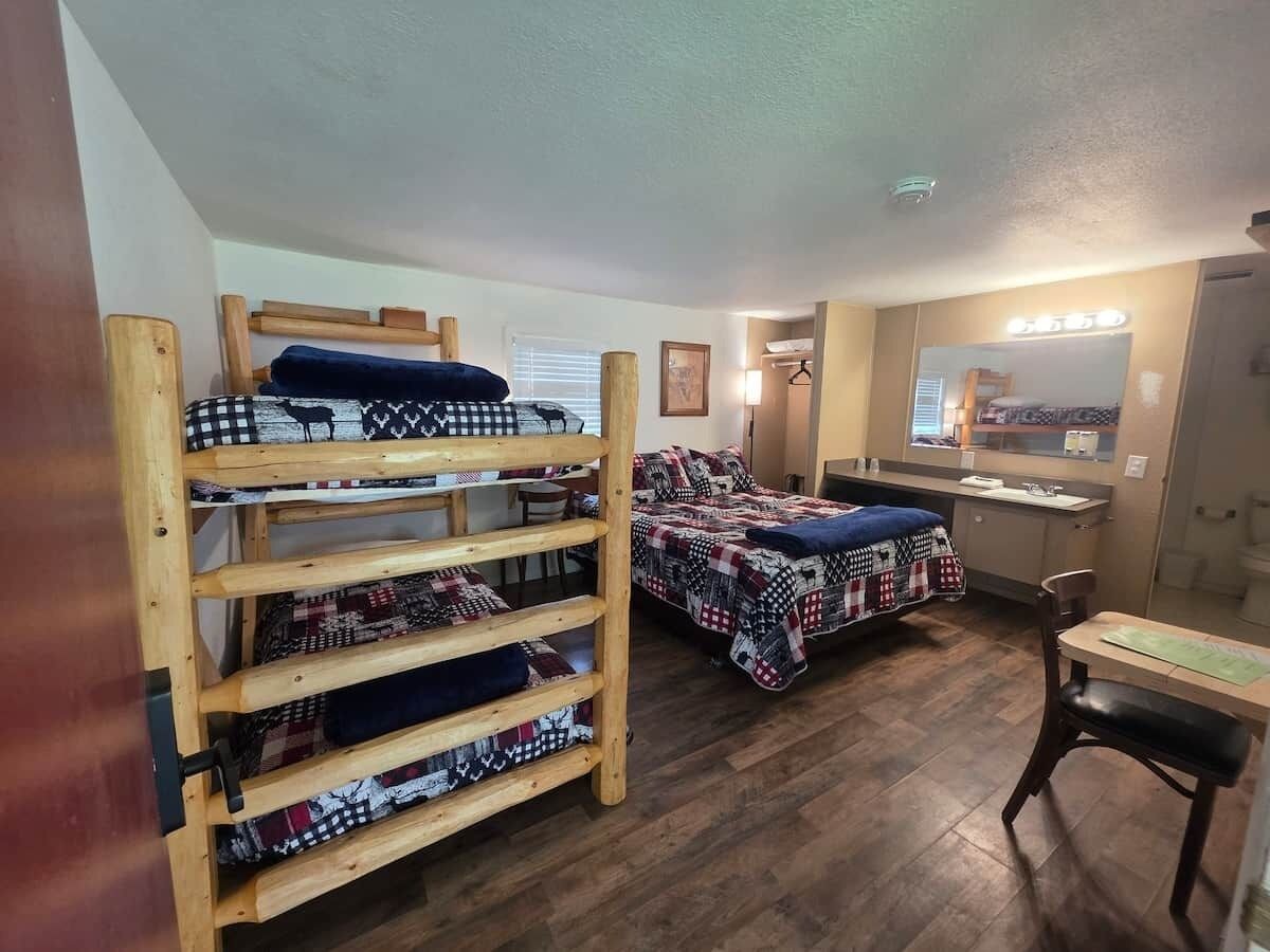A dormitory room with bunk beds, a desk, a chair, and a small kitchenette.