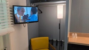 Pieni huone, jossa on seinälle asennettu televisio, keltainen tuoli, puinen pöytä ja pieni keittopiste.