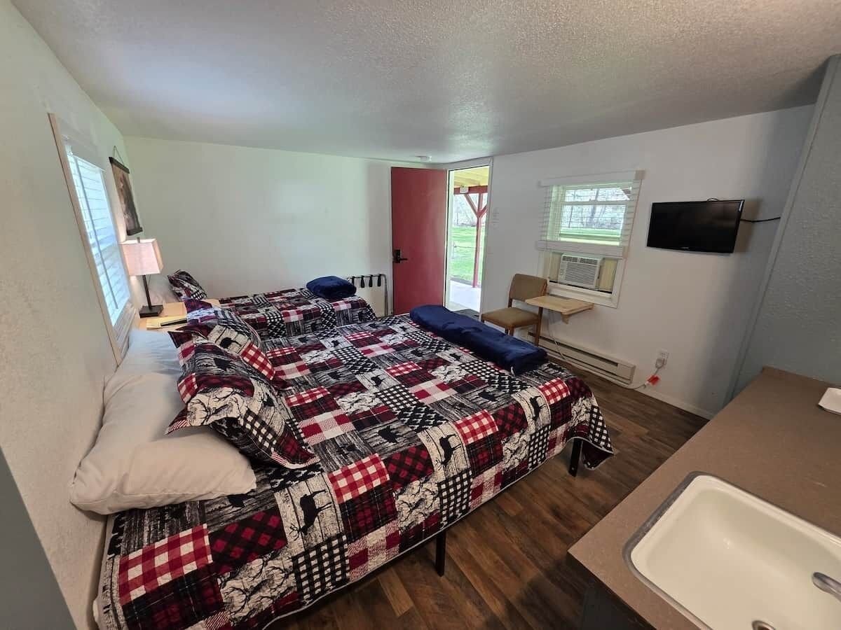 A compact room with a bed, a sink, a television, and a door leading outside.