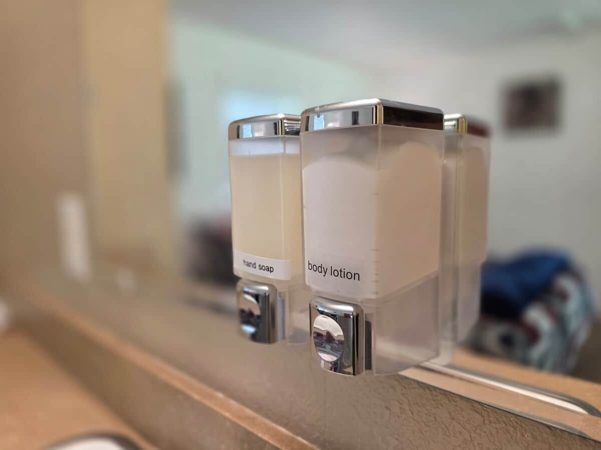 A bathroom with a hand soap dispenser and a body lotion dispenser mounted on a wall.