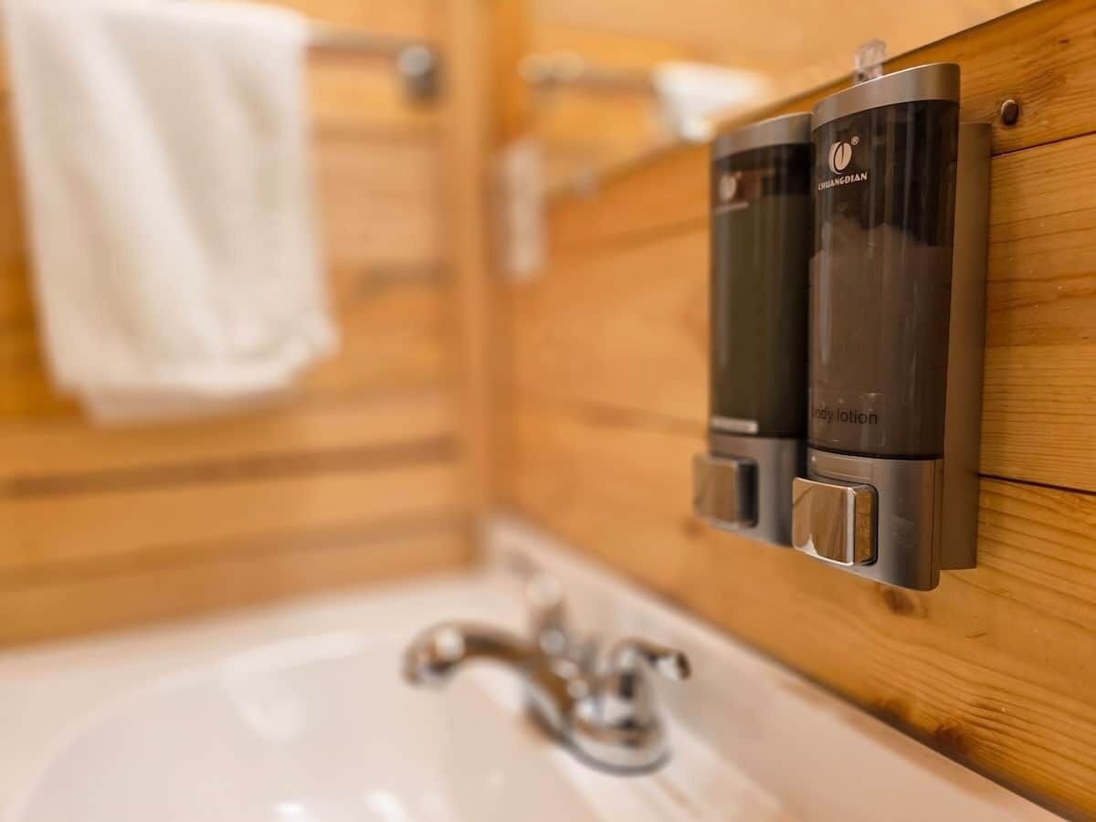 A bathroom with a wooden vanity, a white sink, and two body lotion dispensers.