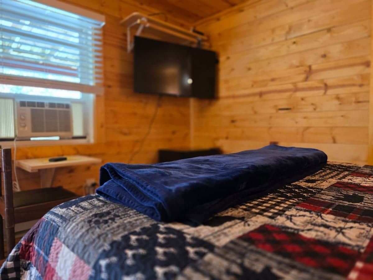 A room with a bed, a television mounted on the wall, and a window with blinds.