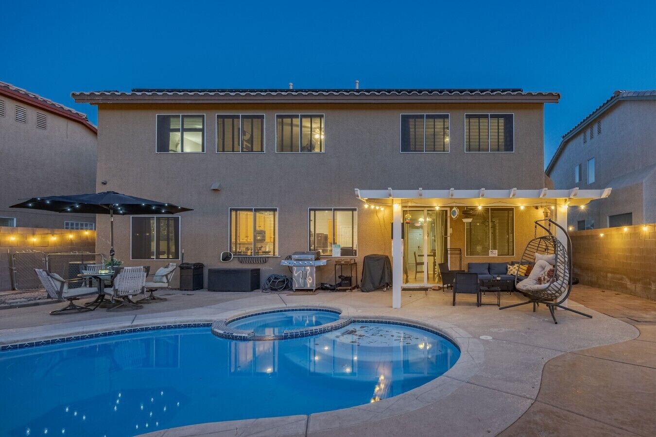 Una casa con piscina, mobiliario de exterior y un patio cubierto.
