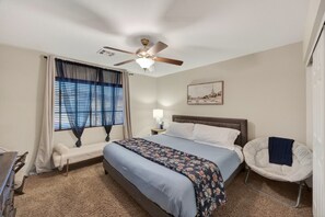 Ein Schlafzimmer mit einem Bett, einem Sessel, einem Deckenventilator und einem Fenster mit Vorhängen.