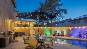 Um quintal com piscina, área de estar externa, luzes de festa e pérgola.
