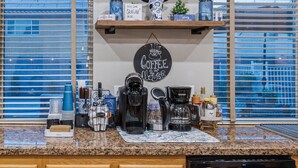 Uma cozinha com equipamentos para fazer café, um letreiro com tema de café e uma janela com persianas.