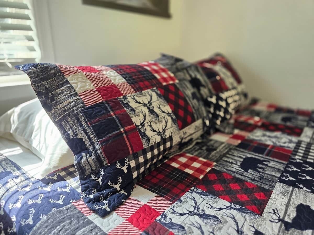Un lit avec une couette et des oreillers ornés d’un motif à carreaux et d’un motif de cerf.