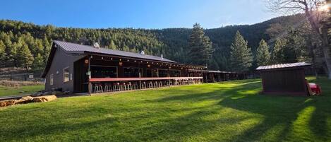 A large building with a covered outdoor seating area, surrounded by a grassy field and trees.