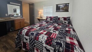 A bedroom with a bed, a desk, a chair, a mirror, and a window with blinds. - 7R Guest Ranch - Room 12 (Pet Friendly) (Lewis and Clark County)