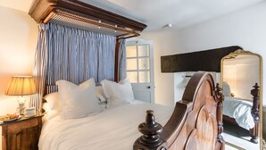 A bedroom with a canopy bed, a bedside table with a lamp, a mirror, and a door with frosted glass panels.