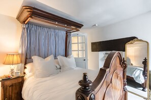 A bedroom with a canopy bed, a bedside table with a lamp, a mirror, and a door with frosted glass panels.