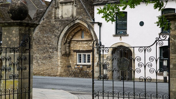 A gated entrance to a building with a stone facade and a white wall with a window.