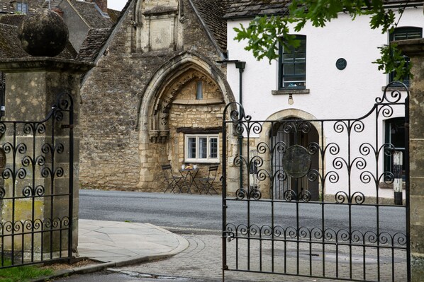 A gated entrance to a building with a stone facade and a white wall with a window.