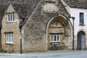 Ein Steinhaus mit traditionellem Bogenfenster, einem kleinen Tisch mit Stühlen davor und einem Straßenschild mit der Aufschrift 'ST JOHN STREET'.