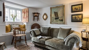 A cozy living room with a sofa, a wooden chair, a small table, and a window with curtains.