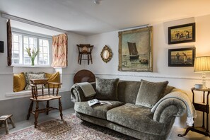A cozy living room with a sofa, a wooden chair, a small table, and a window with curtains.