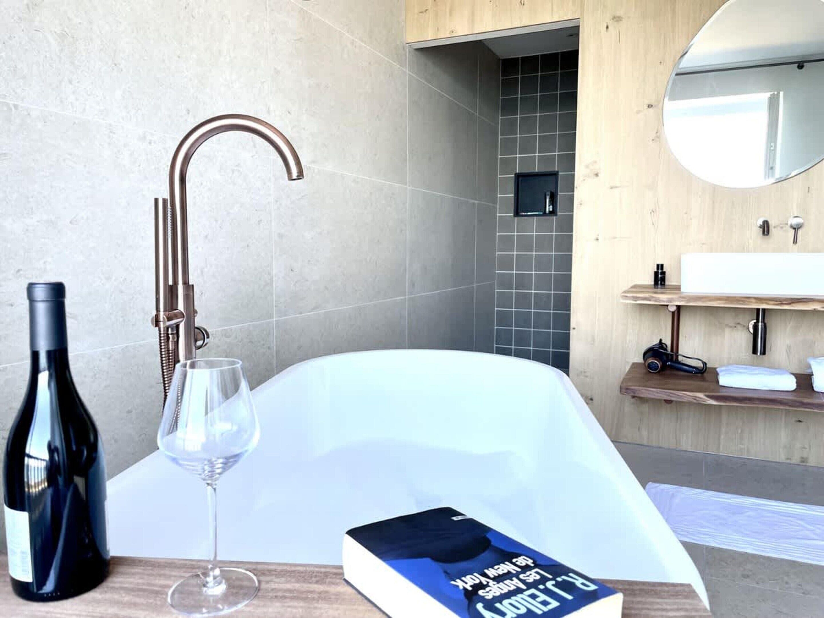 A modern bathroom with a bathtub, a wine bottle, and a glass on the counter.