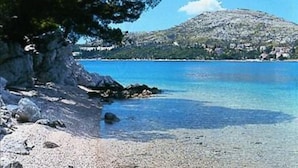 Eine Küstenlandschaft mit blauem Meer, felsigem Ufer und einem Hügel mit Gebäuden im Hintergrund.