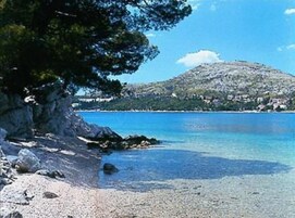 Un paisaje costero con mar azul cristalino, costa rocosa y una colina con edificios al fondo.