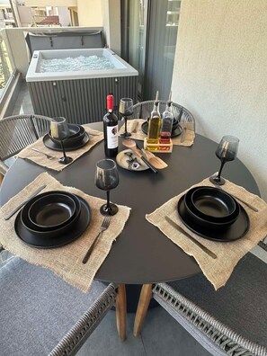 A round table set for two with black plates, wine glasses, and a bottle of wine, surrounded by wicker chairs. - Artion jacuzzi Villa Nikiti a 3-bedroom apartment with jaccuzi in charmingNikiti (Nikiti)