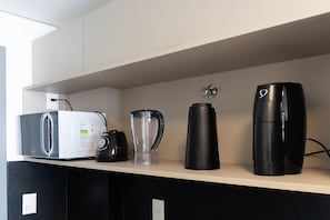 Ein Küchenregal mit einer Mikrowelle, einem Mixer, einer Kaffeemaschine und einem hohen, schwarzen Gerät, möglicherweise eine Kaffeemaschine oder ein Espressokocher.