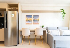 A modern kitchen with a stainless steel refrigerator, a dining area with two chairs, and a grey sofa. - AT Self #804 Steps From the Beach by Carpediem (João Pessoa)