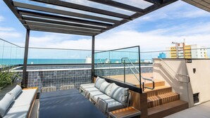 A rooftop terrace with a glass balustrade, outdoor seating, and a view of the sea. - AT Self #804 Steps From the Beach by Carpediem (João Pessoa)
