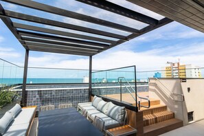 A rooftop terrace with a glass balustrade, outdoor seating, and a view of the sea. - AT Self #804 Steps From the Beach by Carpediem (João Pessoa)