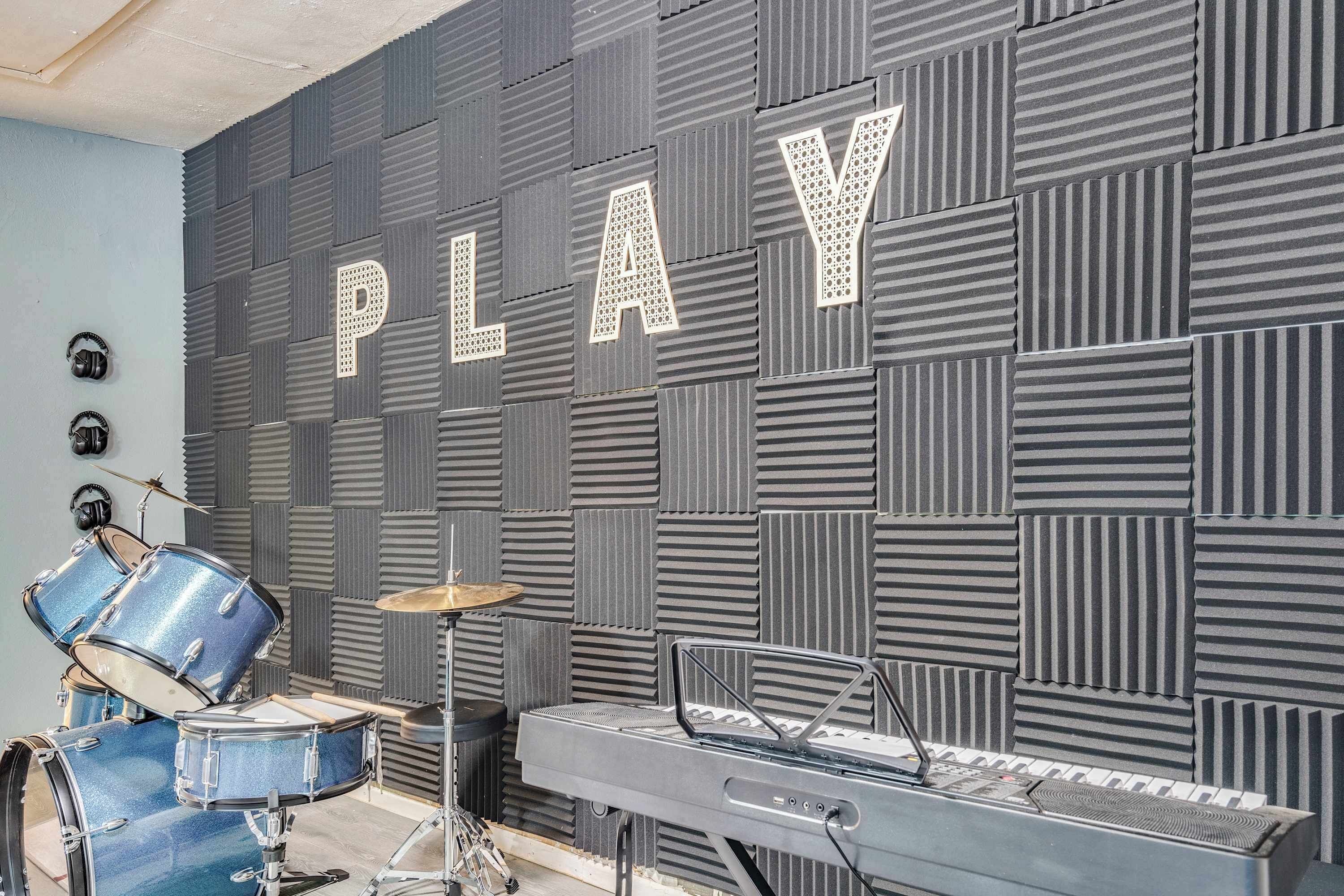 A music studio with a wall-mounted keyboard, a drum set, and a microphone.